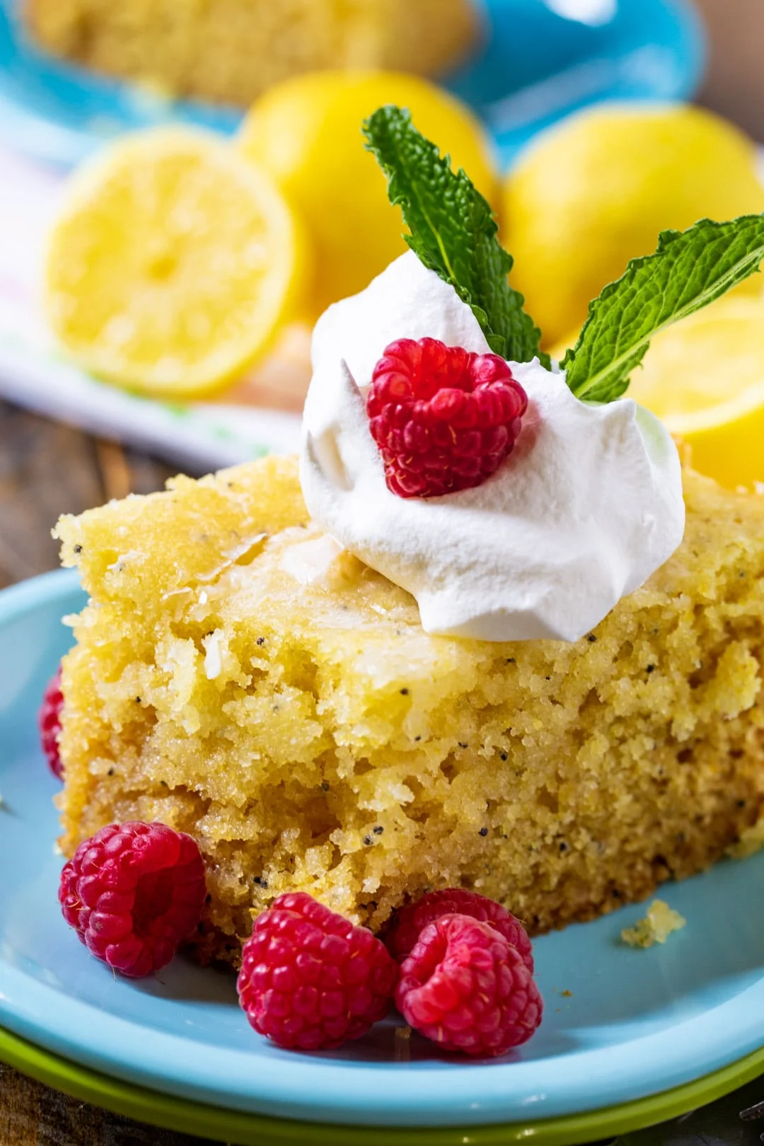 Slice of lemon cake on blue plate with fresh raspberries.