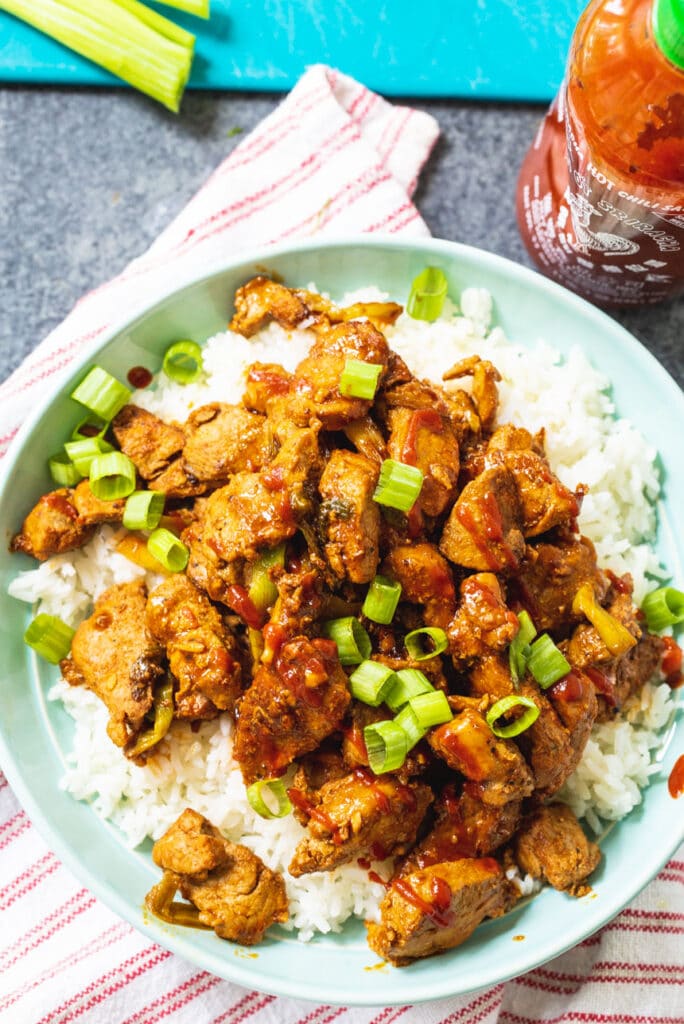 Stir-Fried Spicy Pork over rice with bottle of Sriracha sauce.