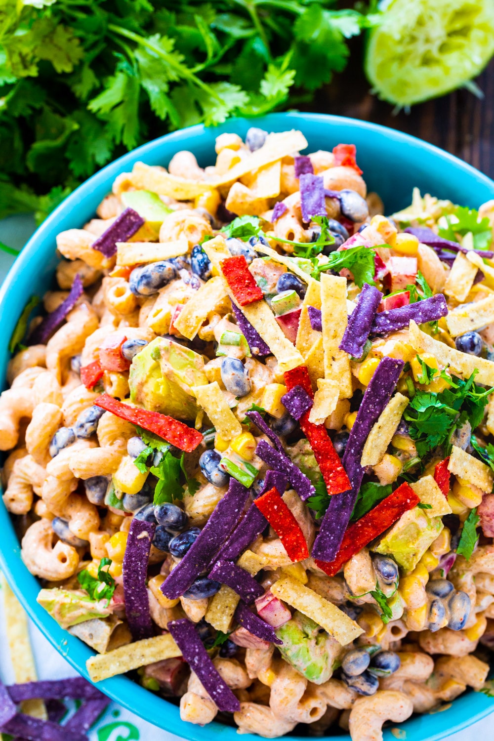 Pasta salad in a blue bowl with bunch of cilantro beside it.