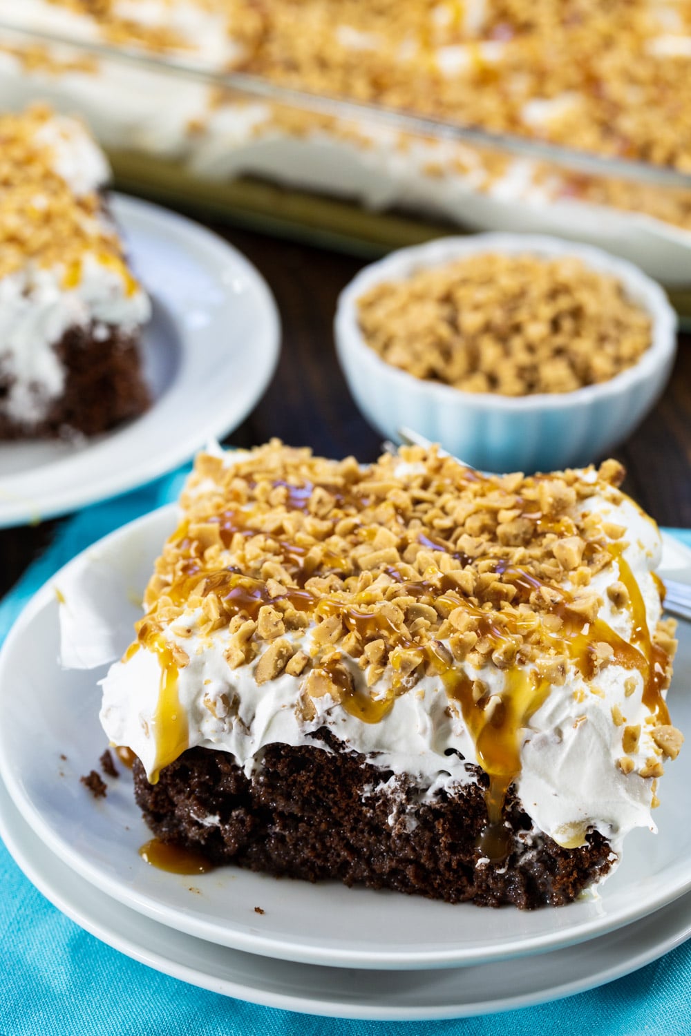 Slice of poke cake with bowl full of toffee bits in background.