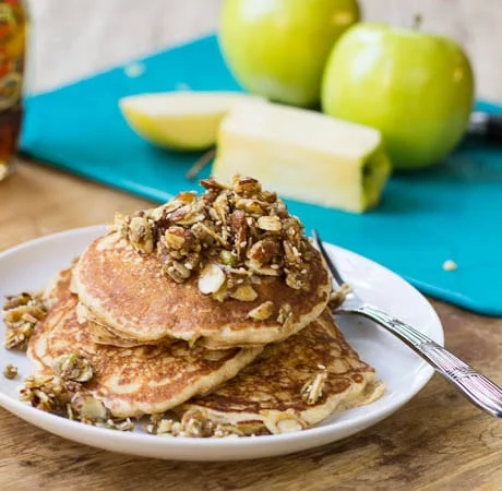 Apple Pancakes with Nutty Topping on a plate with Golden Delicious apples in background.