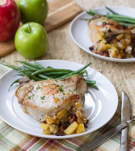 Pork Chops Stuffed with Apple and Bacon on a white plate with green beans. Apples in background.