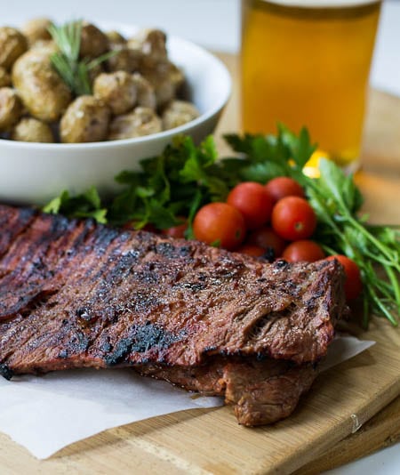 Bloody Mary Skirt Steak on wood cutting board with cherry tomatoes and parsley.