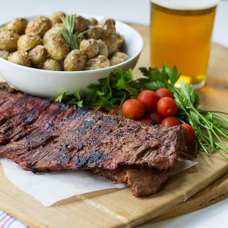 Skirt Steak on cutting board with bowl of roasted potatoes and a beer.