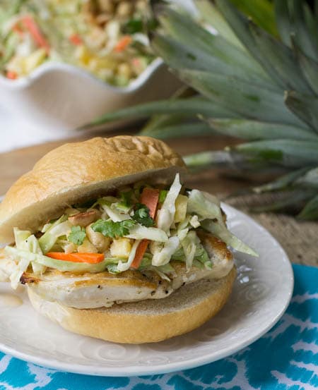 Chicken Sandwich with Pineapple Slaw on a plate with bowl of slaw in background.