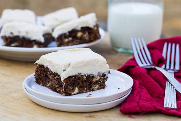 A single brownie on a small white plate with more brownies and milk in background.