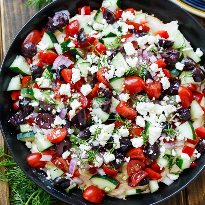 Creamy Greek Dip with cream cheese, hummus, tomatoes, cucumber, olives, feta, and fresh dill.