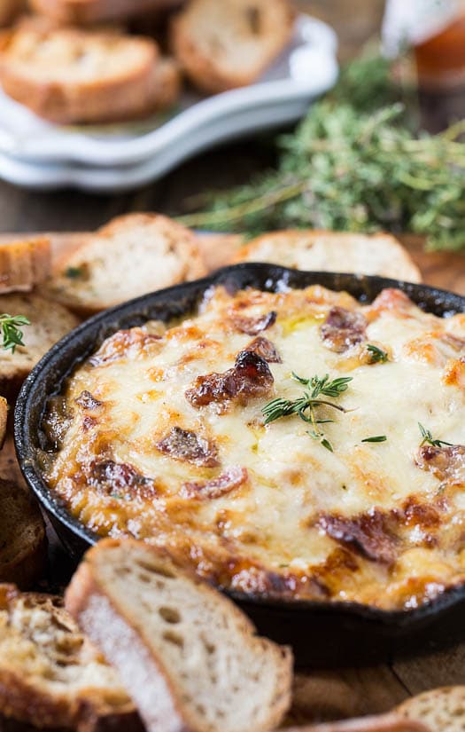Onion Dip with Bacon and Gruyere surrounded by thyme and fresh baguette slices.