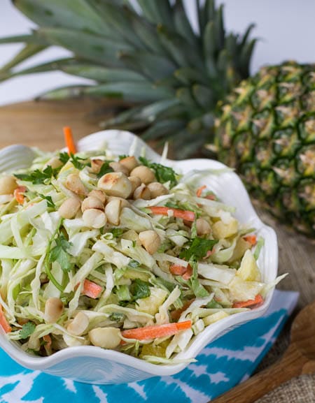 Pineapple Macadamia Slaw in white serving bowl with whole pienapple in background.