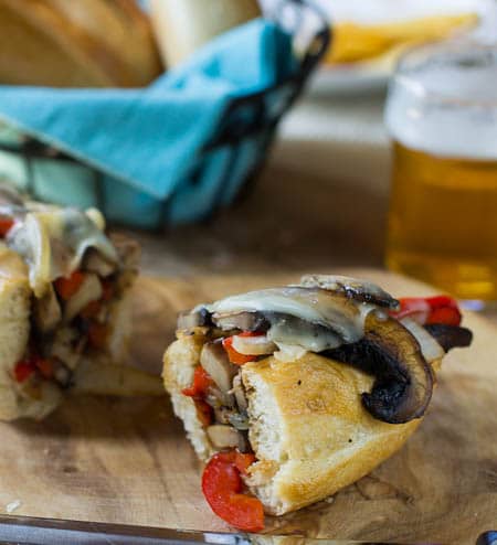 Half of a vegetarian Cheesesteak on a wood board with beer in background.