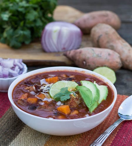 Posole in a white bowl with sweet potatoes and cilantro in background.