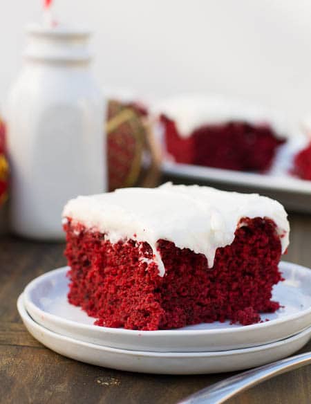Red Velvet Cake on a plate with jug of milk in background.