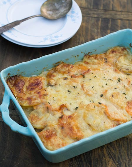 Caramelized Onion and Potato Gratin in blue baking dish with plates and spoon beside it.