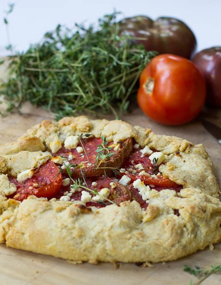 Tomato Galette on wood cutting board with fresh thyme and tomatoes in background.